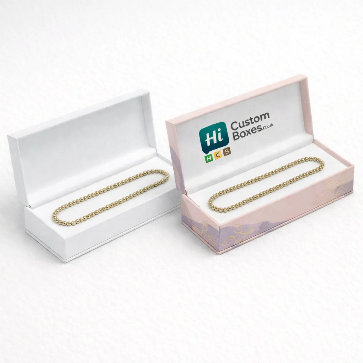 Elegant white and pink hinged boxes displaying gold beaded anklets on soft white padded inserts-